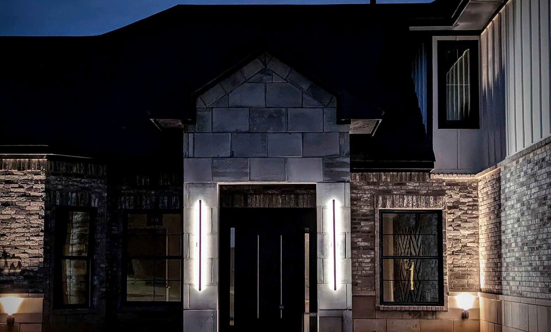 Stone entry with modern pivot door and vertical lights at dusk, built by Cincero Homes